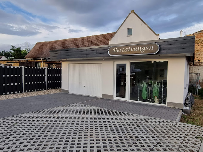 Ein Bestattungsinstitut mit weißer Fassade und Schaufenster, verbunden mit wölkigem Himmel.